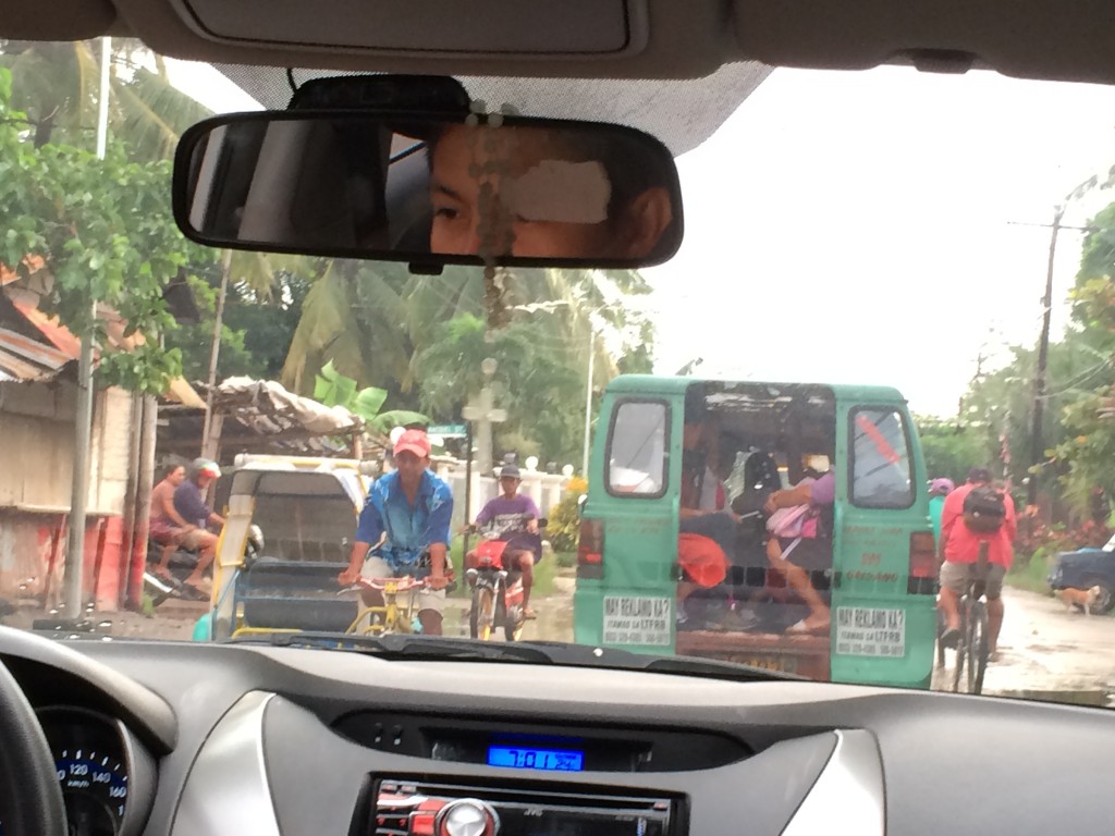 Blick aus dem Auto: Tricycle und Motorrad von vorn; grüner Jeepney und Fahrrad von hinten